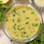 Bright yellow salad dressing in a small glass bowl with chopped fresh parsley on top.