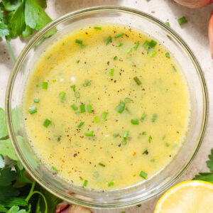 Light yellow vinaigrette in a small glass bowl garnished with fresh chives and black pepper.