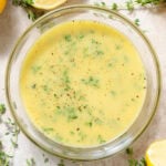 Bright yellow vinaigrette with fresh thyme in a glass bowl with lemons and thyme around the bowl.