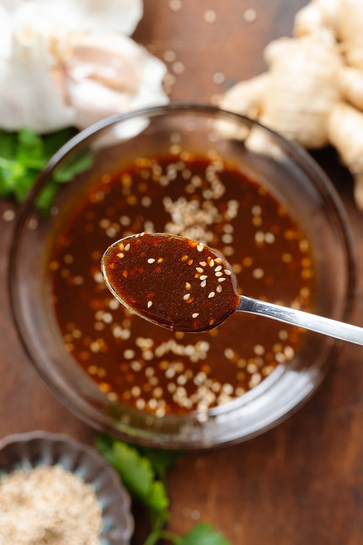 A spoon holding dark brown miso dressing with white sesame seeds over a glass bowl with more of the dressing.