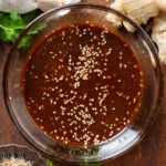 Dark brown miso dressing in a small glass bowl garnished with sesame seeds.