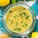 Bright yellow vinaigrette in a small glass bowl garnished with fresh parsley and black pepper.