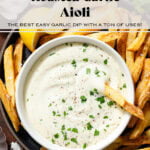 Creamy white dip in a small white bowl garnished with fresh parsley on a black plate with french fries with one fry in the dip.