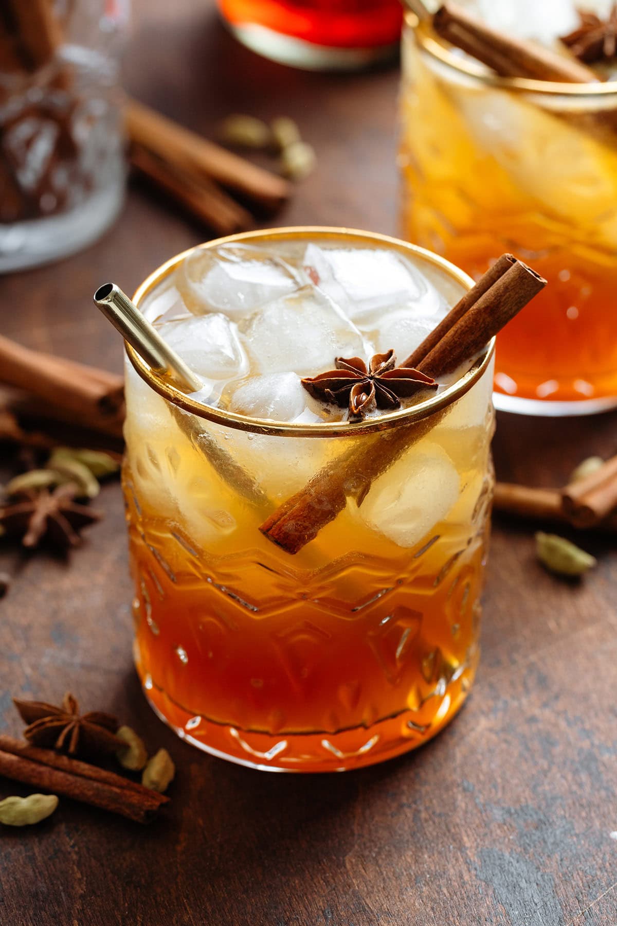 Dark orange cocktail with ice and sparkling water on top for a layered effect in a short glass with a gold rim garnished with a cinnamon stick and star anise.