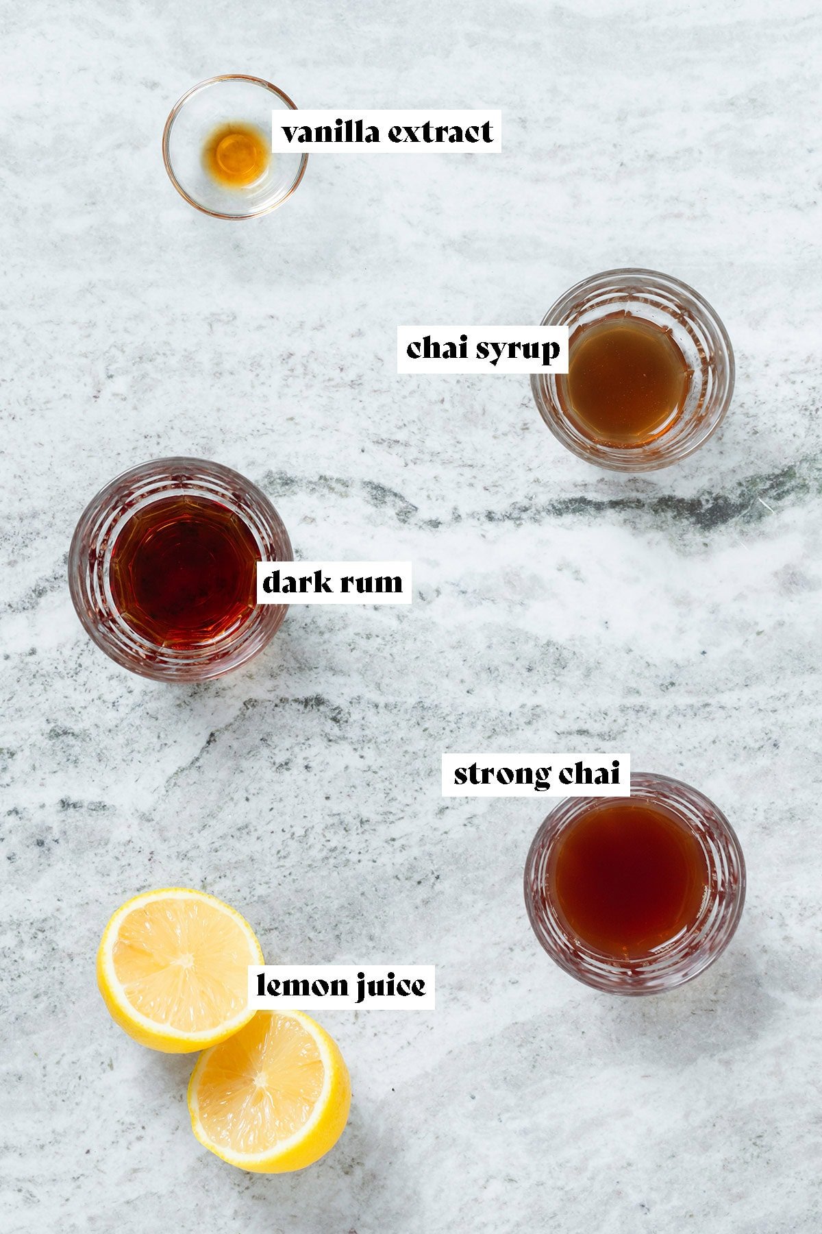 Ingredients like chai, dark rum, and chai syrup laid out measured in small glasses.