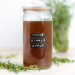 A glass jar with syrup that says thyme simple syrup in embossed letters.