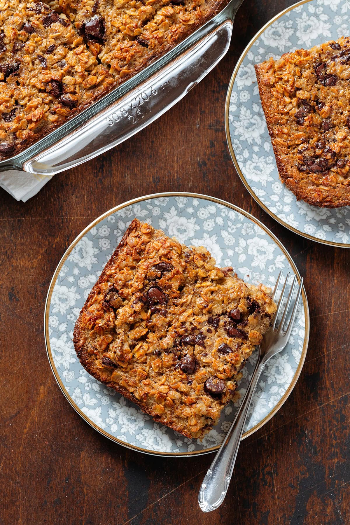 A slice of chocolate chip baked oatmeal on a small blue plate with flowers with a fork on the right.