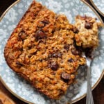 A slice of chocolate chip baked oatmeal on a small blue plate with flowers with a fork on the right holding a bite of the oatmeal.