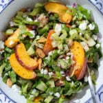 Peach and romaine lettuce salad with goat cheese and sliced almonds in a white bowl with a blue rim and a fork inserted on the right.