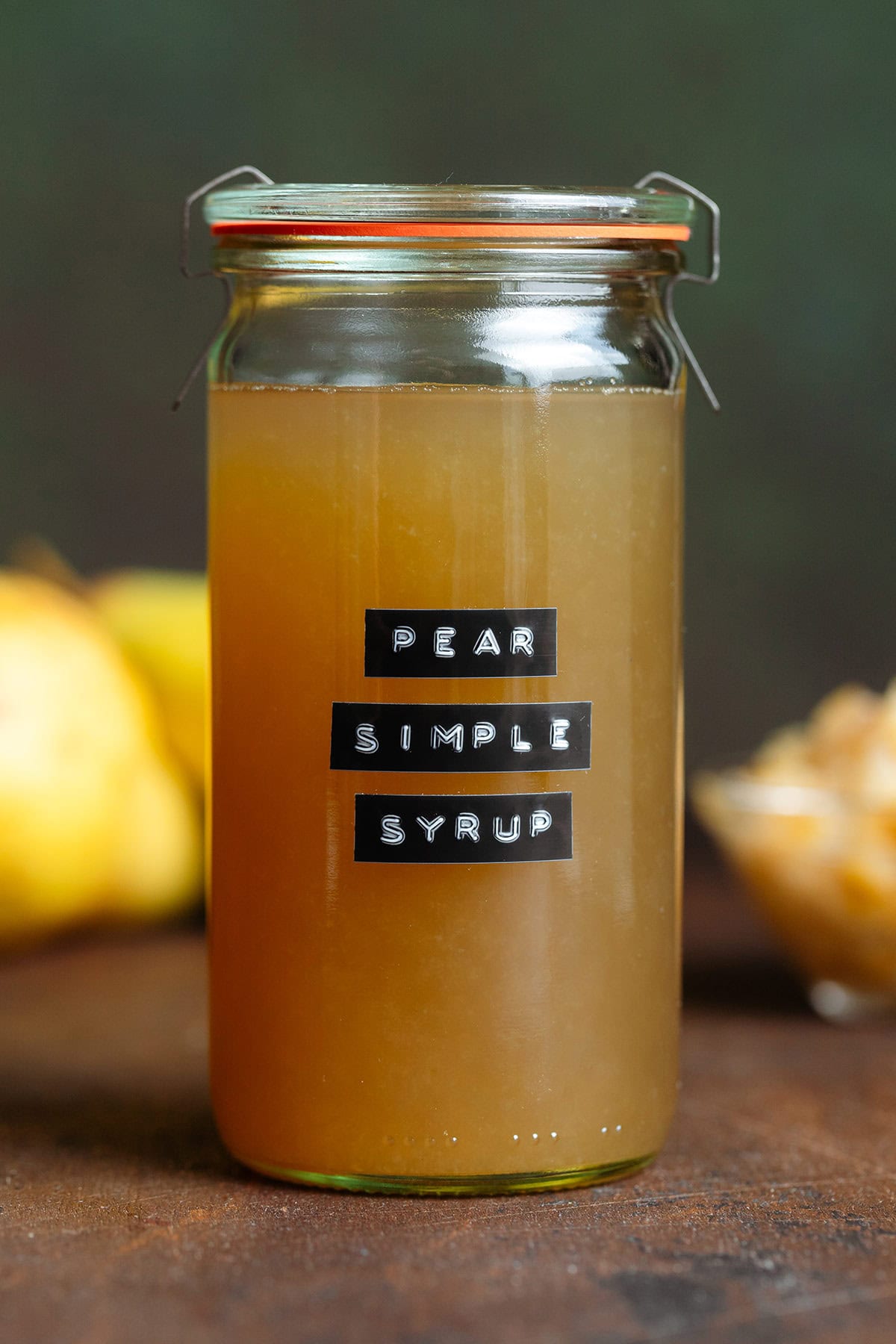 Dark yellow syrup in a glass jar with a lid and a black embossed label that says pear simple syrup on a dark brown background.