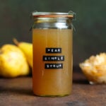 Dark yellow syrup in a glass jar with a lid and a black embossed label that says pear simple syrup on a dark brown background.