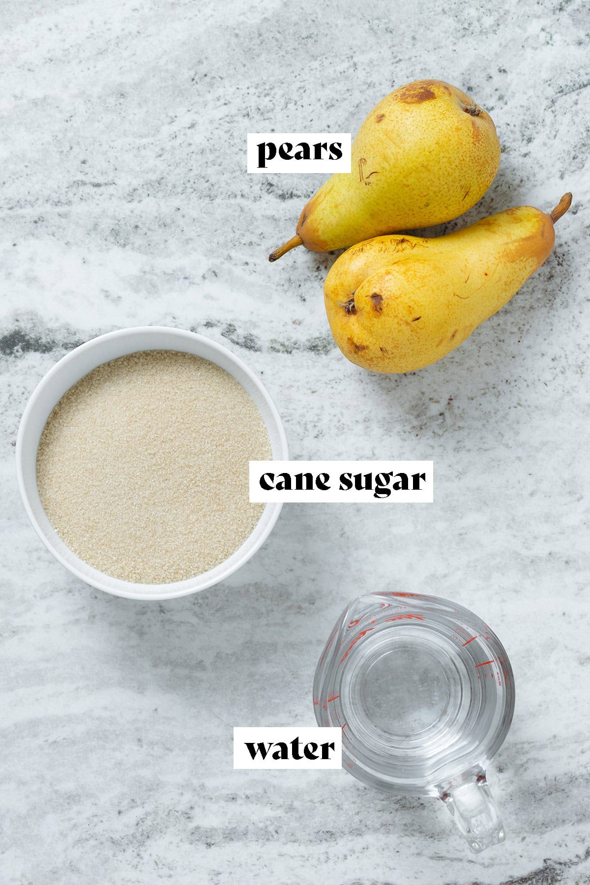 Cane sugar in a bowl, water in a glass measuring cup, and two pears on a grey stone background.