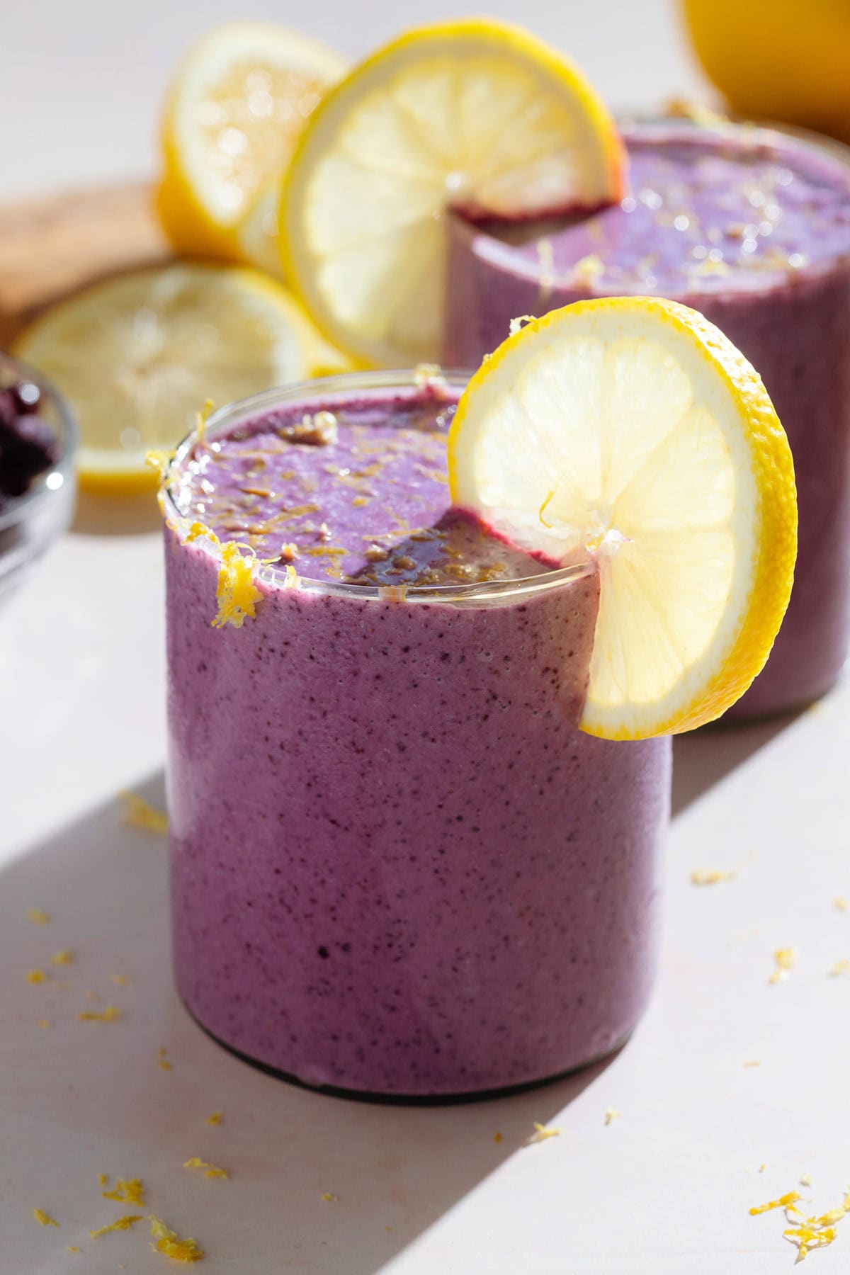 Bright purple smoothie in a short glass garnished with a slice of lemon and fresh lemon zest.