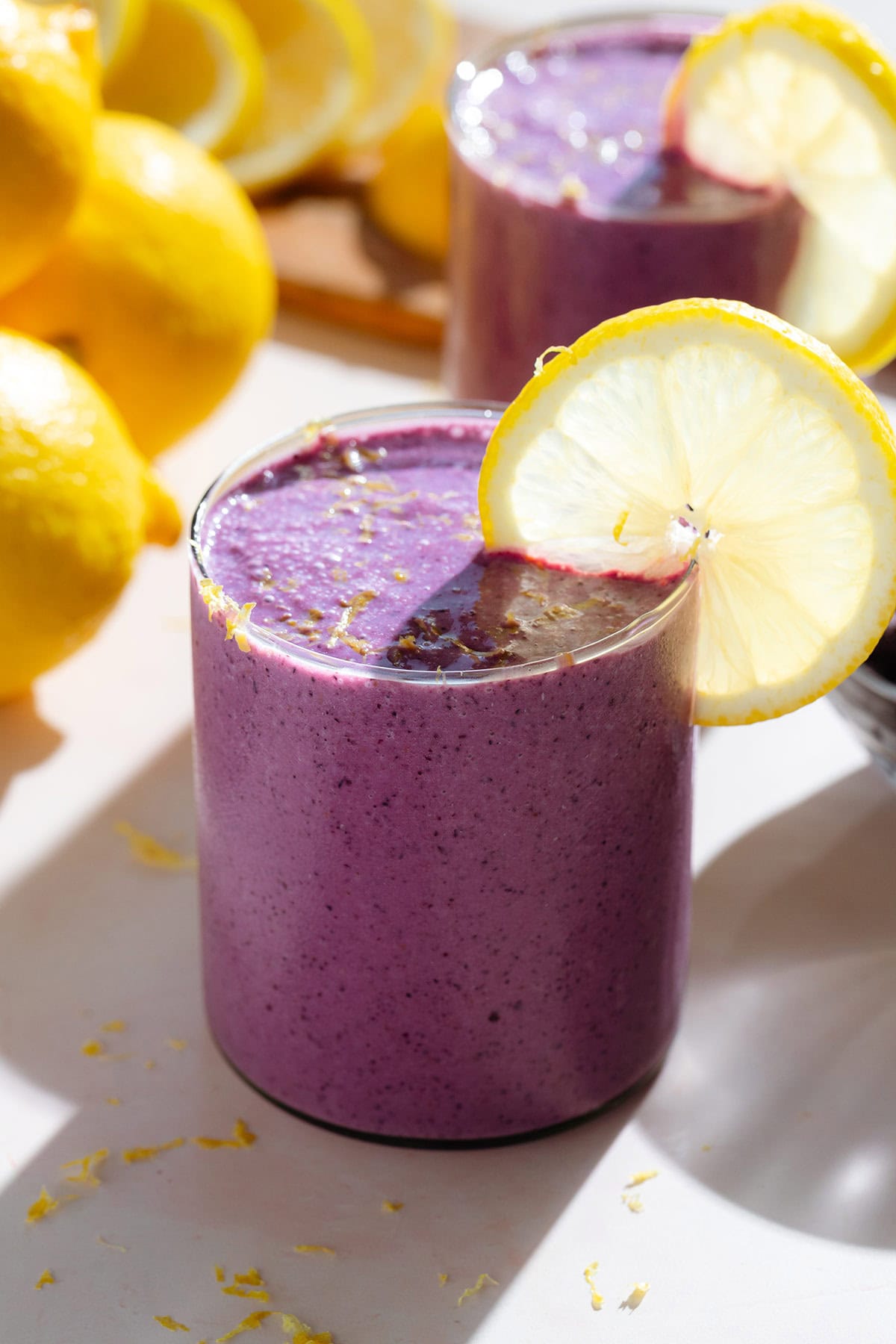 Bright purple smoothie in a short glass garnished with a slice of lemon and fresh lemon zest.