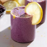 Bright purple smoothie in a short glass garnished with a slice of lemon and fresh lemon zest.