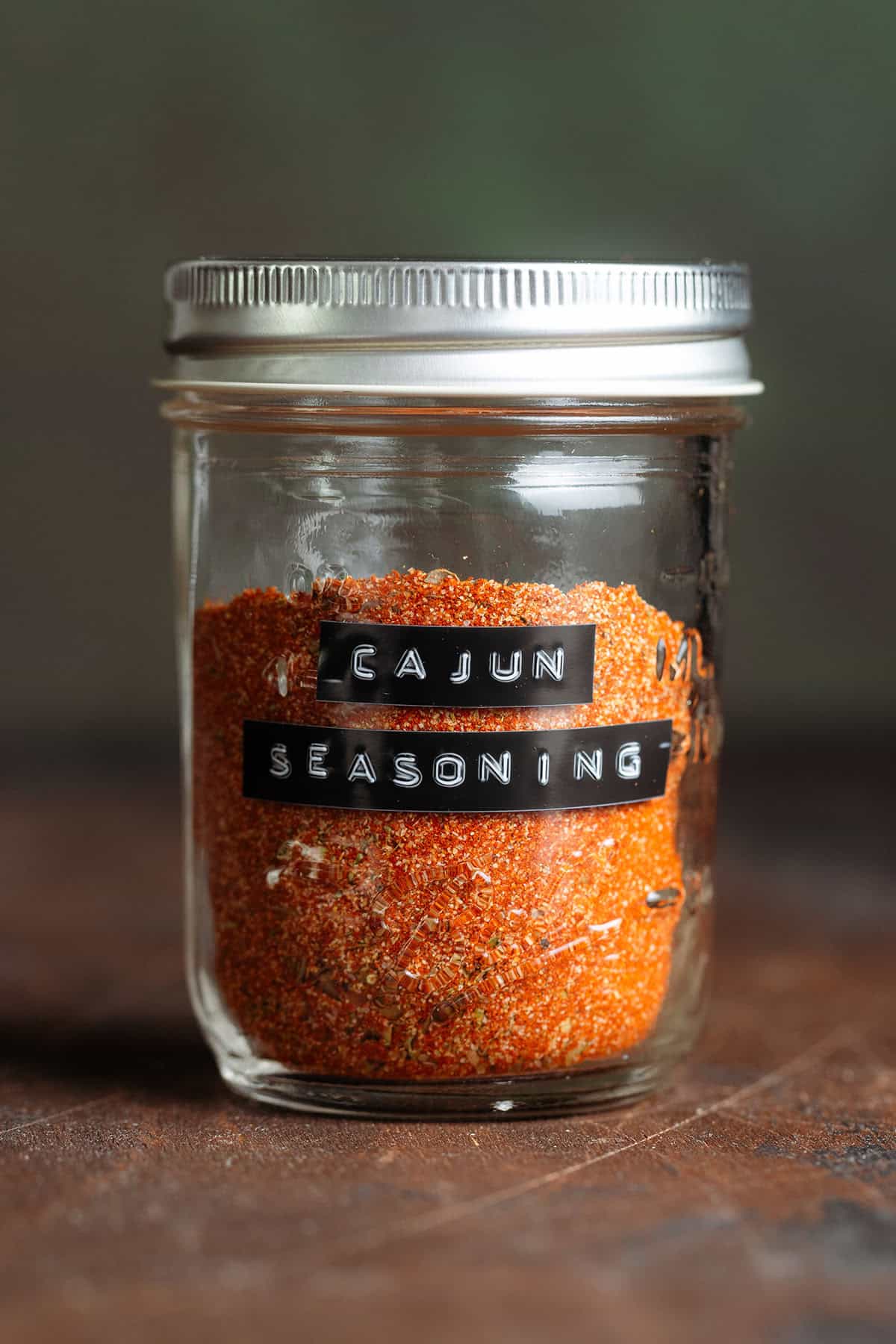 Bright red cajun spice in a glass jar with a black embossed label.