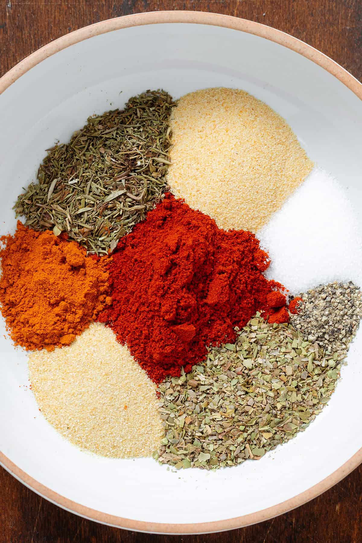 Spices like paprika, oregano, thyme, garlic powder, and sea salt in a white bowl with an orange rim.