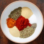 Spices like paprika, oregano, thyme, garlic powder, and sea salt in a white bowl with an orange rim.