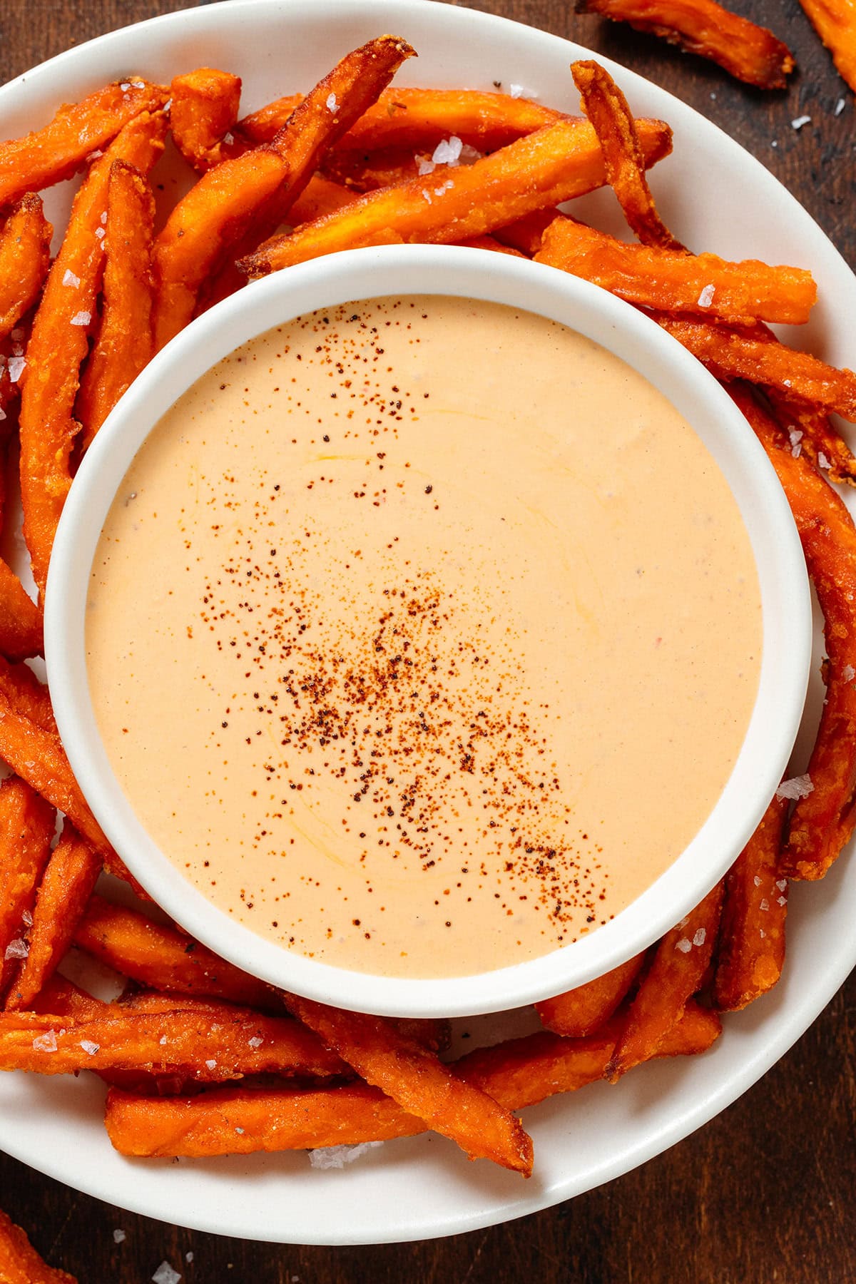 Creamy orange sauce in a white bowl on a plate of sweet potato fries.