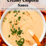 Creamy chipotle sauce in a small white bowl on a plate of sweet potato fries garnished with black pepper and chopped chives.