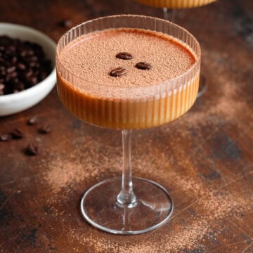 A coupe glass with creamy espresso mocktail dusted with cacao and garnished with three coffee beans.