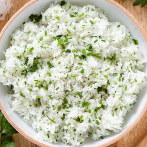 Basmati rice cooked with finely chopped fresh herbs in a white bowl with an orange rim.