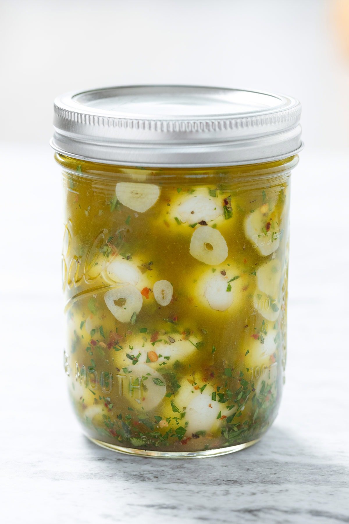 Marinated small mozzarella balls in olive oil and fresh herbs in a glass jar.