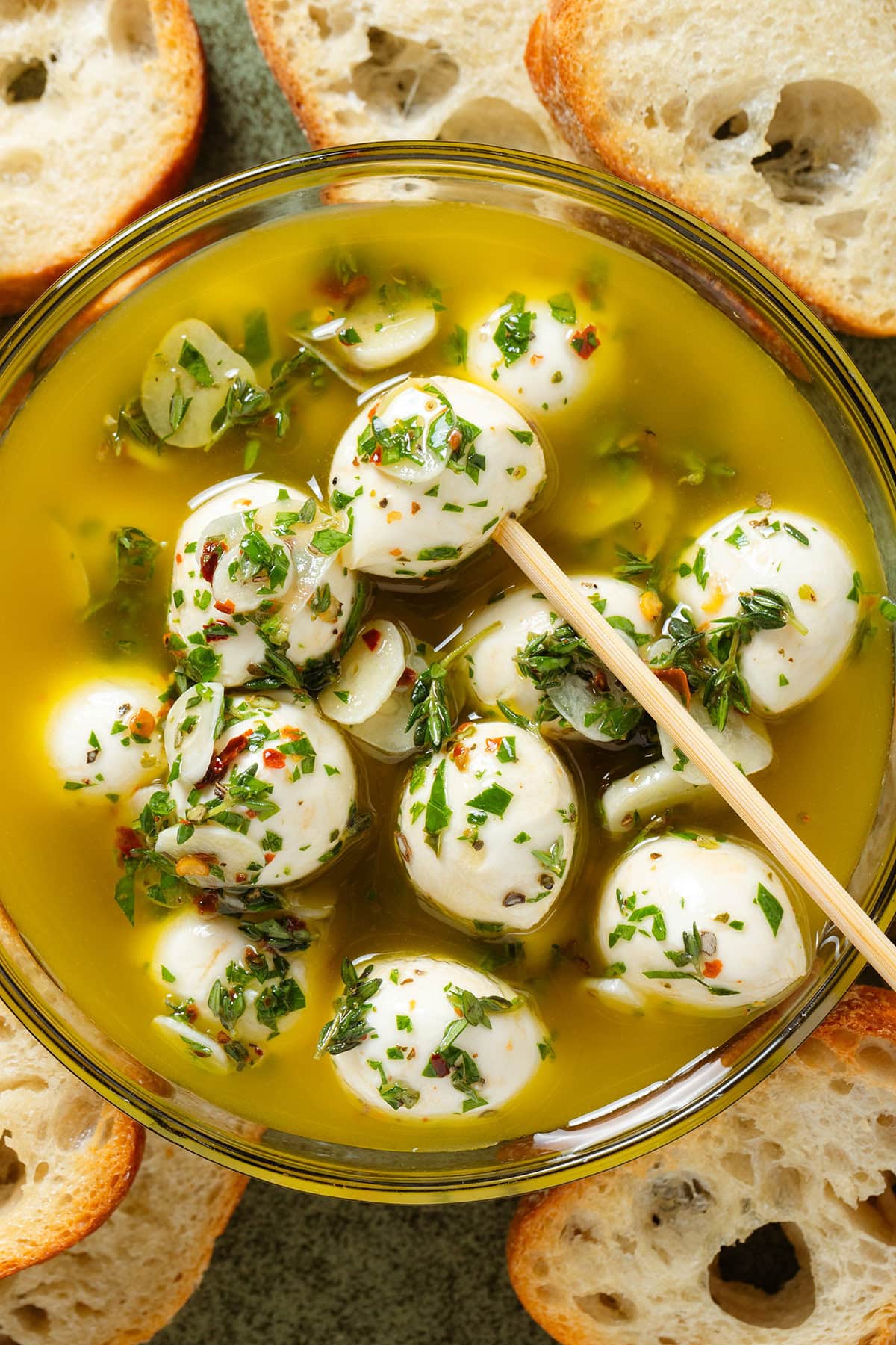 Marinated small mozzarella balls in olive oil and fresh herbs in a glass bowl with a bamboo stick in.