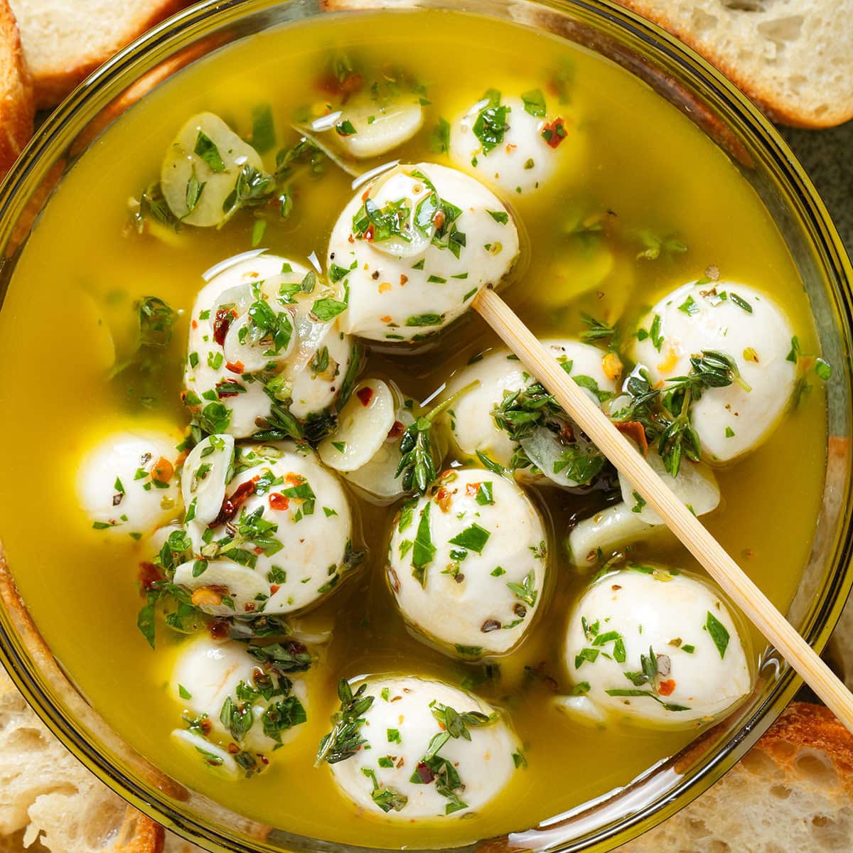 Marinated small mozzarella balls in olive oil and fresh herbs in a glass bowl with a bamboo stick in.