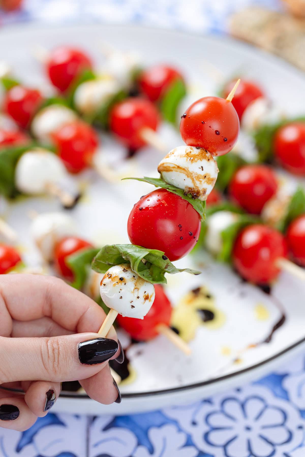 A hand holding a wooden skewer with cherry tomatoes, mini mozzarella, and fresh basil.