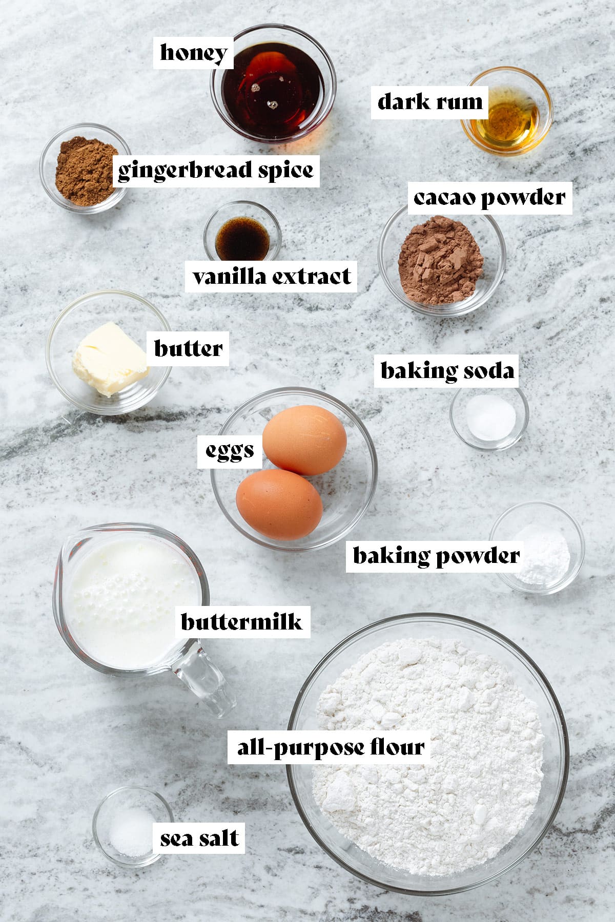 Ingredients like flour, buttermilk, cacao powder, honey, butter, vanilla extract and baking powder all measured and laid out in small glass bowls with text overlay.