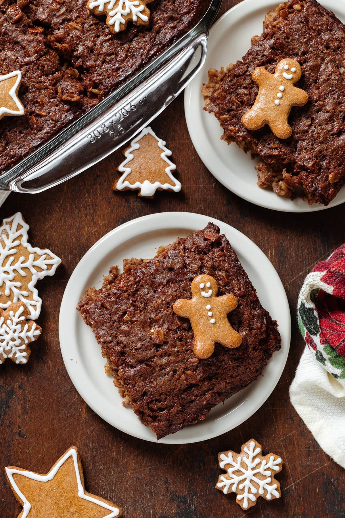 Two squares of baked oatmeal on small white plates garnished with a small gingerbread man cookies and more cookies around the plates.