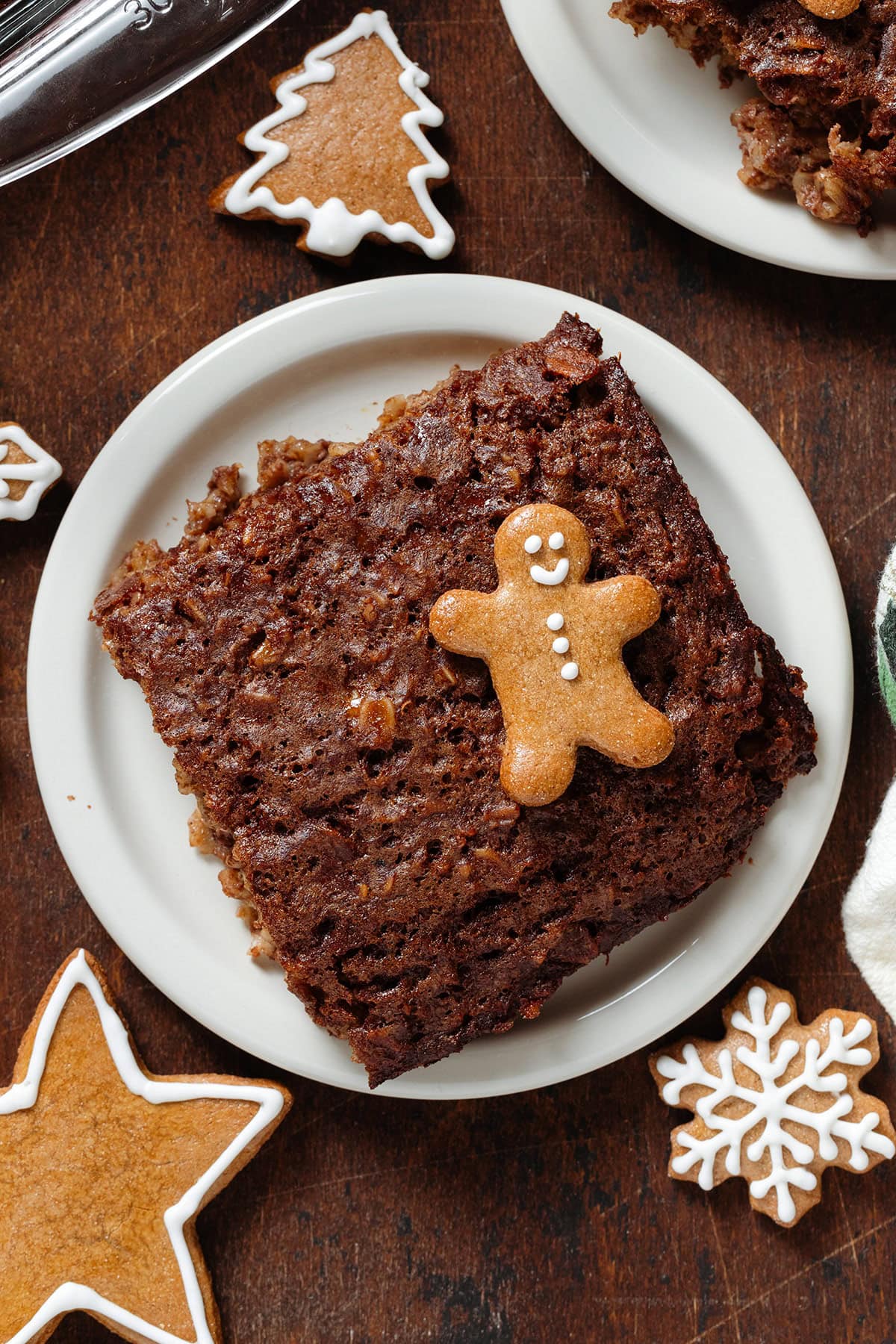 A square of baked oatmeal on a small white plate garnished with a small gingerbread man cookie and more around the plate.