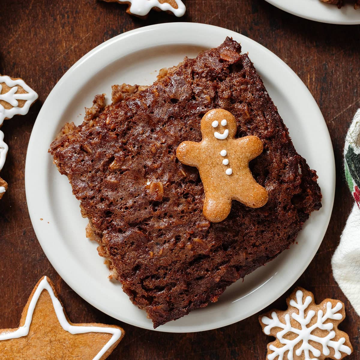 A square of baked oatmeal on a small white plate garnished with a small gingerbread man cookie and more around the plate.