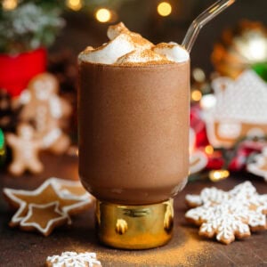 Creamy dark brown gingerbread smoothie topped with whipped cream and cinnamon in a tall glass with a short thick gold stem with a glass straw.