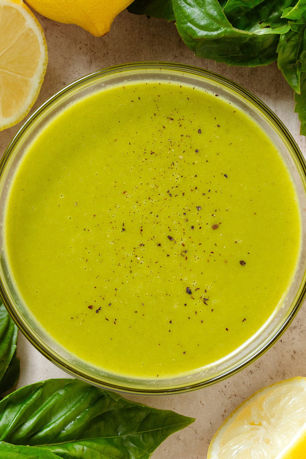 Bright green vinaigrette in a small glass bowl sprinkled with black pepper.