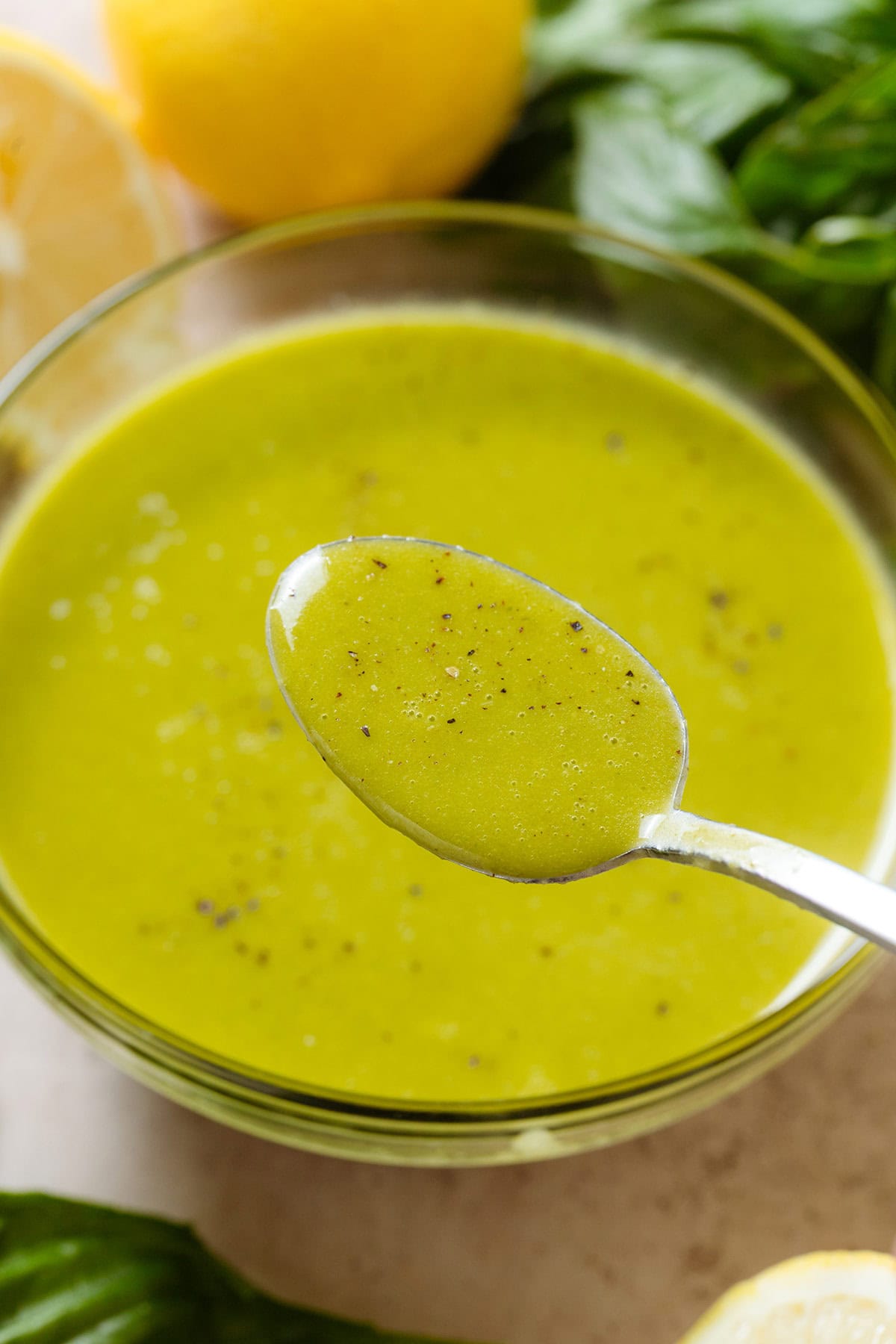 Bright green vinaigrette in a small glass bowl sprinkled with black pepper and a spoon scooping up the vinaigrette.