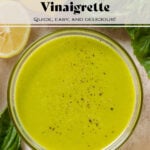 Bright green vinaigrette in a small glass bowl sprinkled with black pepper and with fresh basil and lemons around the bowl.