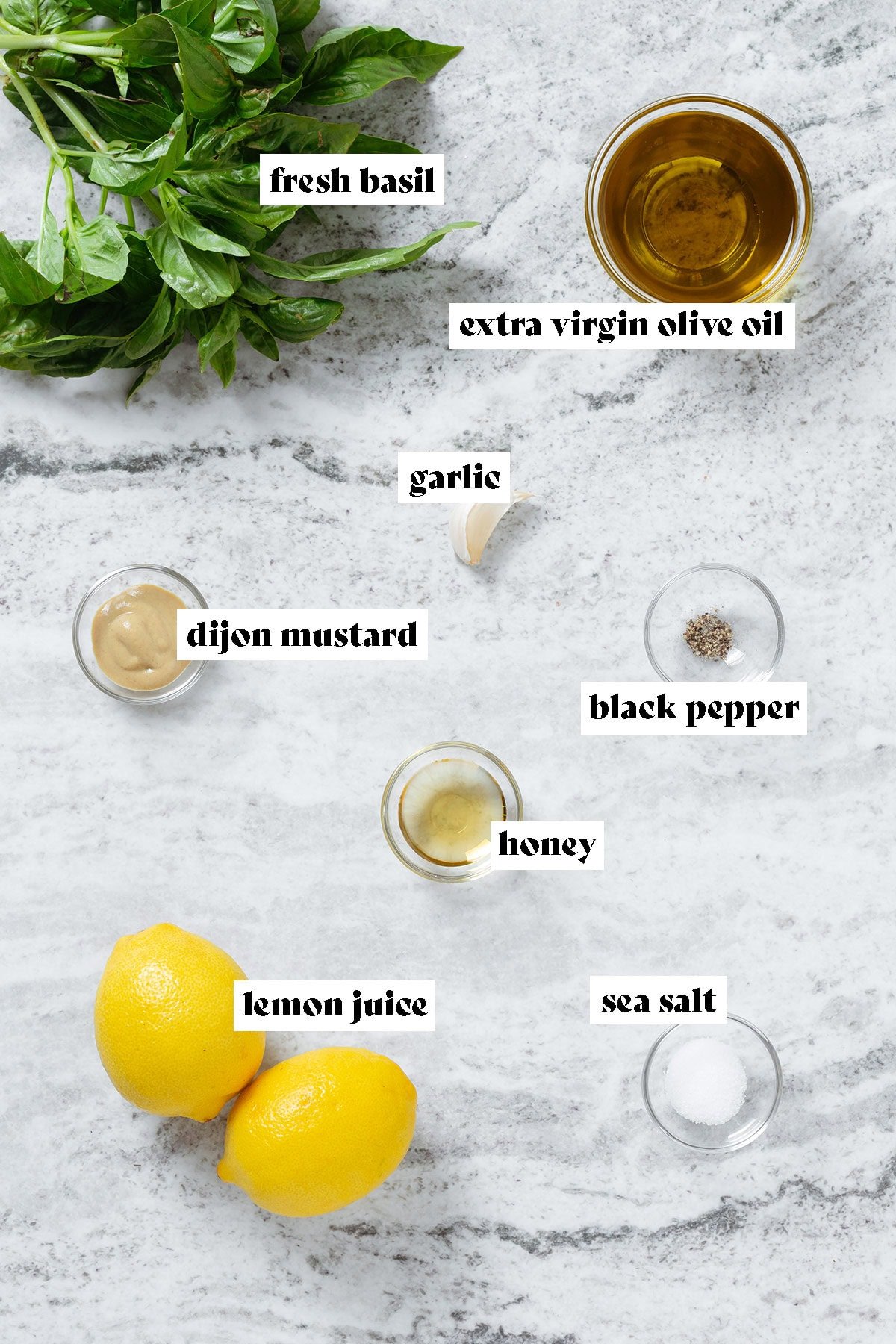 Fresh basi, two lemons, and olive oil, honey, dijon mustard, and spices in small glass bowls with text overlay.