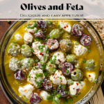 Marinated olives and crumbled feta in olive oil and spices in a glass bowl with toothpicks on the side.