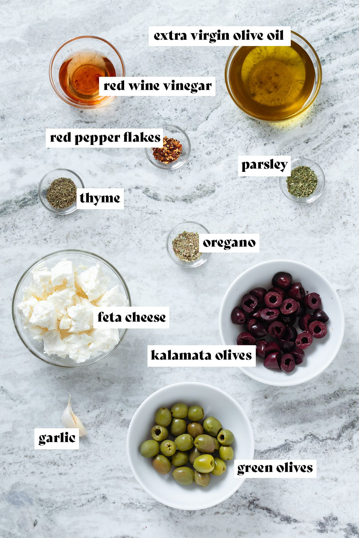 Feta, olives, olive oil, vinegar, and spices measured in small bowls with text overlay.