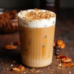 Iced latte in a tall glass with cold foam and finely chopped caramelized pecans on top.