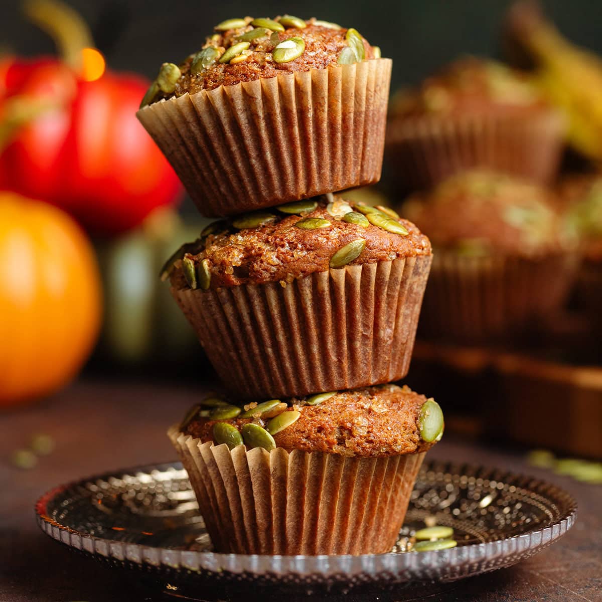 Three muffins with pumpkin seeds on top stacked on a small brown glass plate.