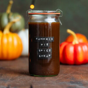 Dark brown pumpkin syrup in a glass jar with pumpkins in the background.