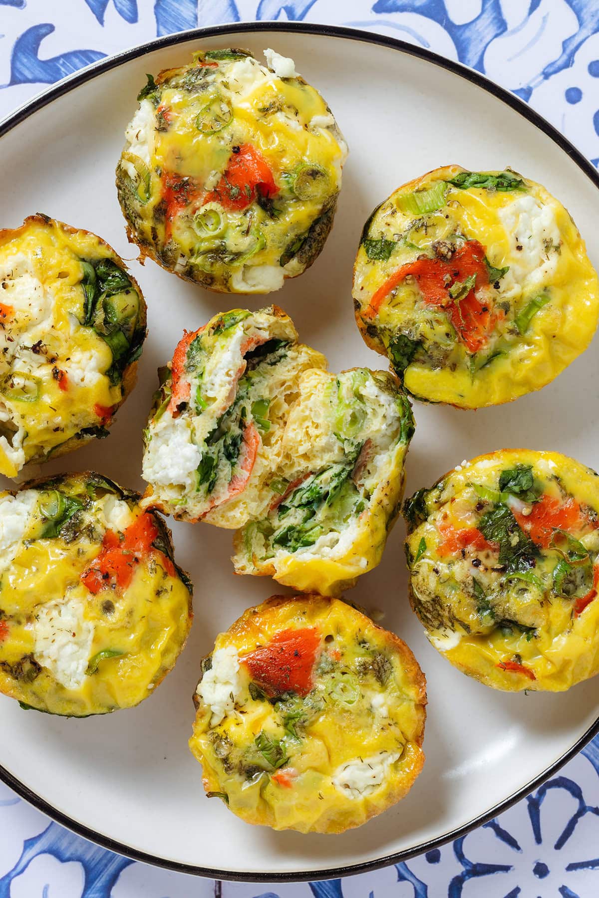 Egg muffins with smoked salmon, cream cheese, and spinach on a white plate with the muffin in the middle cut in half to show the inside.