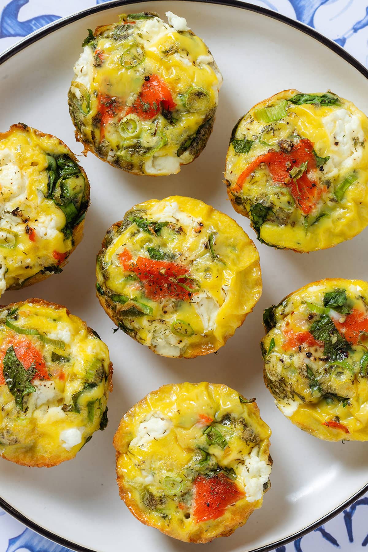 Egg muffins with smoked salmon, cream cheese, and spinach on a white plate with a black rim.