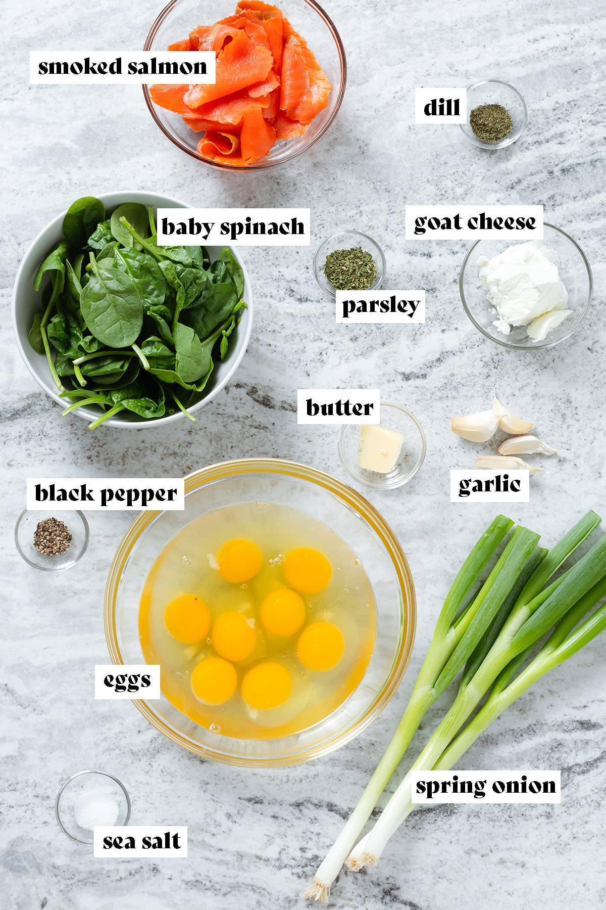 Eggs in a large glass bowl, spring onions, baby spinach, smoked salmon, and spices in small bowls with text overlay.