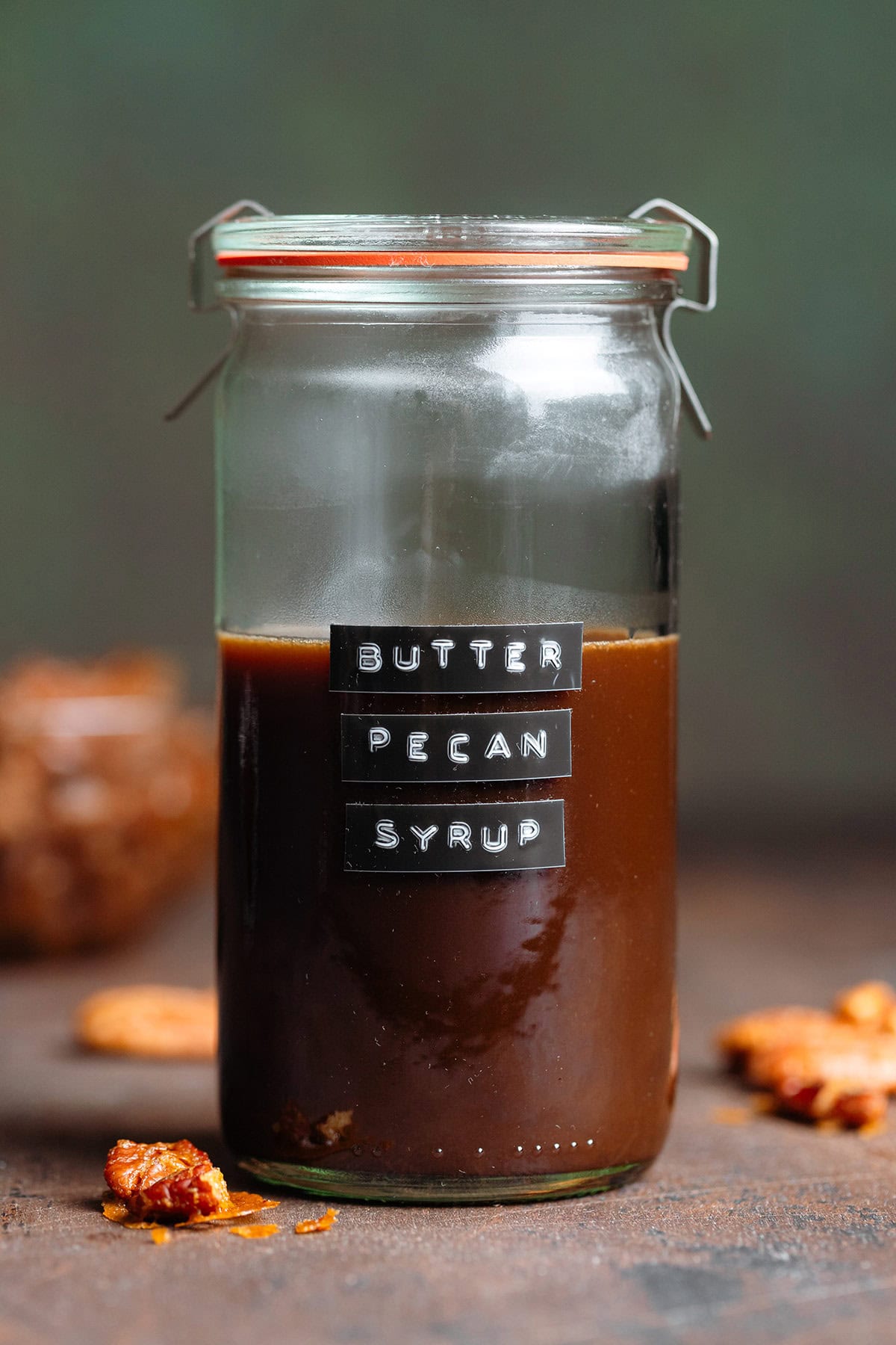 A glass jar with dark brown syrup with a black embossed label that says butter pecan syrup.