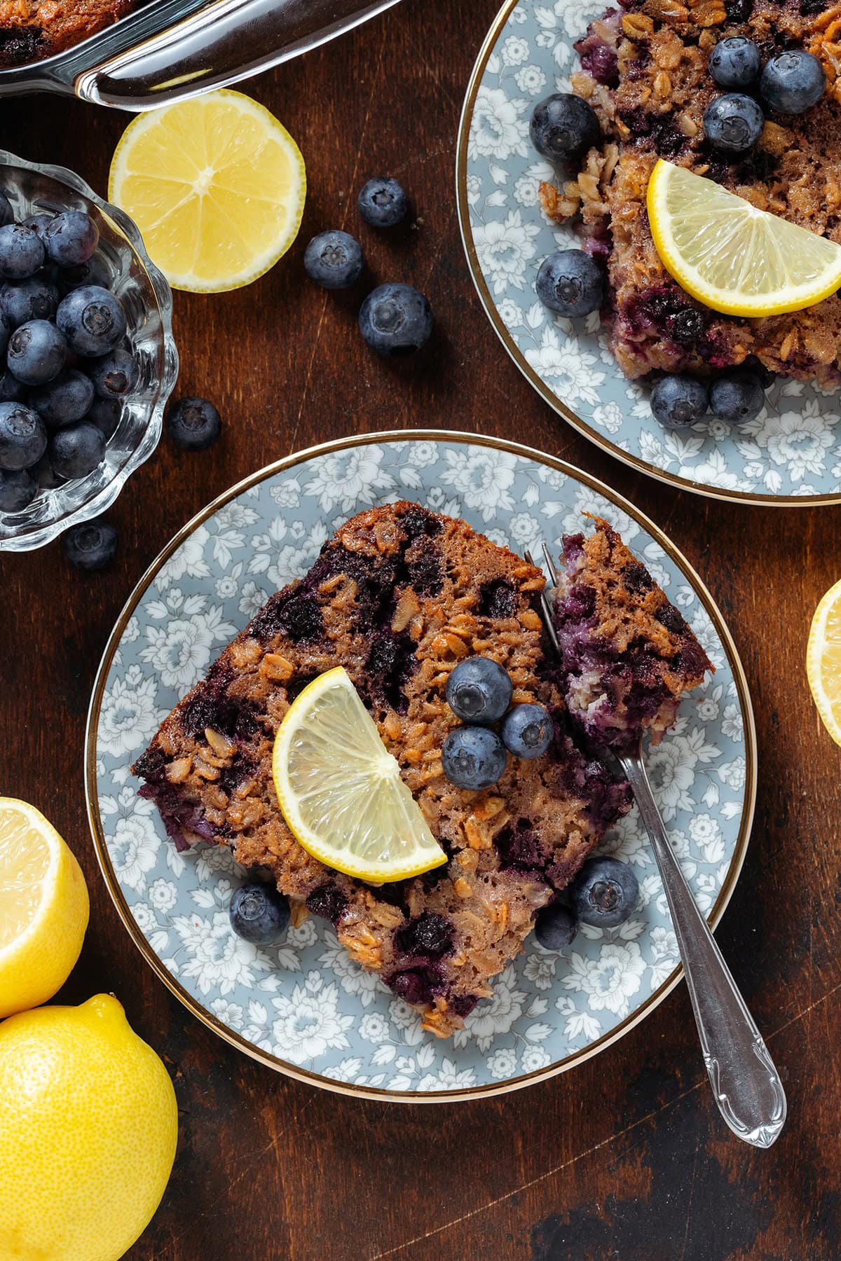 Baked blueberry lemon oatmeal squares on blue plates with gold rim and a fork with a bite of the oatmeal resting on the side of the plate.