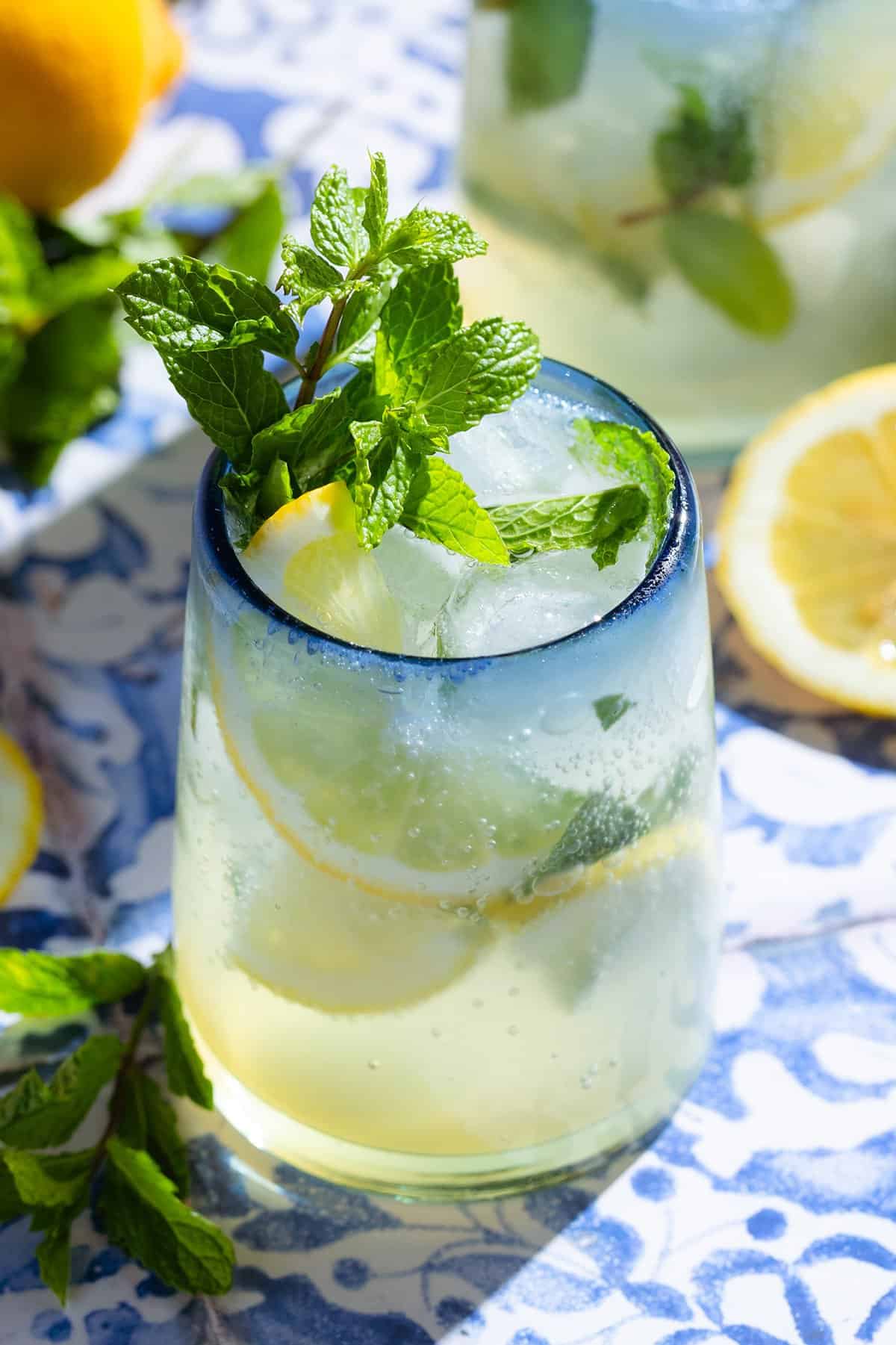 A lemon mocktail in a short glass with a blue rim garnished with lemon slices and fresh mint.